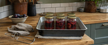 Bradepande med seks henkogte glas blommer i lage på en bordplade i egetræ