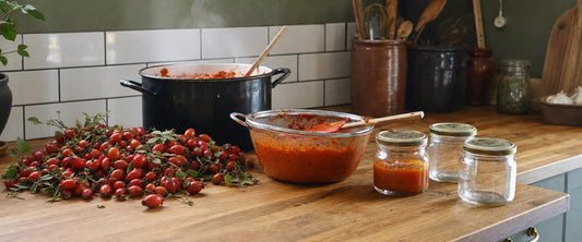Friskplukkede hyben, hybenpuré i en sigte og sylteglas med marmelade på et køkkenbord